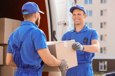 Erkek nakliyeciler sokakta arabadan kutu indiriyor.