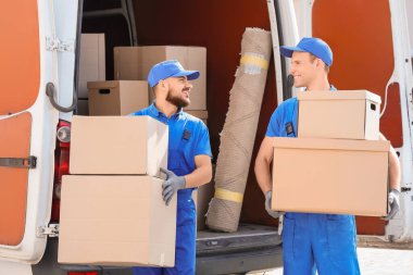 Erkek nakliyeciler sokakta arabadan kutuları boşaltıyor.