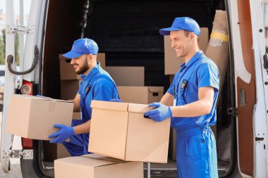 Erkek nakliyeciler sokakta arabadan kutuları boşaltıyor.