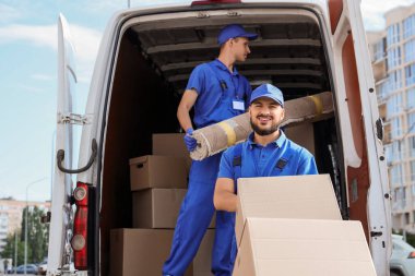 Erkek nakliyeciler arabalarını kutularla ve halılarla sokağa boşaltıyor.