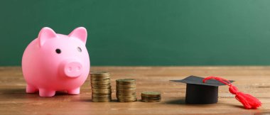 Mezuniyet şapkası ve bozuk paralarla yeşil tahtanın yanındaki masada kumbarada. Öğrenci kredisi kavramı