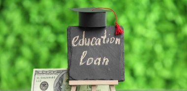 Açık havada yazı tahtasıyla birlikte kredi, mezuniyet şapkası ve dolar banknotları.