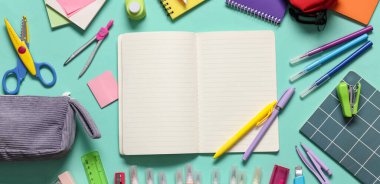 Turkuaz arka planda farklı kırtasiye malzemesi içeren boş bir defter