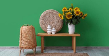 Hasır lambalı şık bir oda ve yeşil duvarın yanında bir vazo ayçiçeği buketi