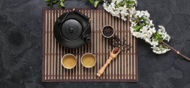 Bardaklı çaydanlık, bir kaşık kuru çay ve siyah grunge arka planda çiçekler.