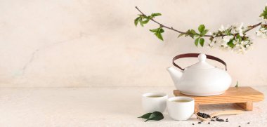 Çaydanlık, fincanlar, bir kaşık kuru çay ve arka planda yapraklar olan ahşap tezgah.