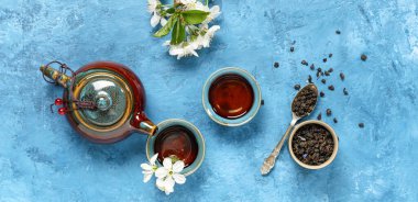 Fincanlı çaydanlık, bir kaşık kuru yeşil çay ve mavi grunge arka planda çiçekler.