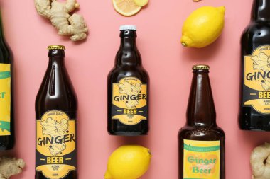 Farklı şişelerde zencefilli bira ve pembe arka planda limonlu kompozisyon.