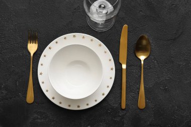 Altın çatal bıçak takımı ve siyah arka planda şarap kadehi olan zarif bir masa.