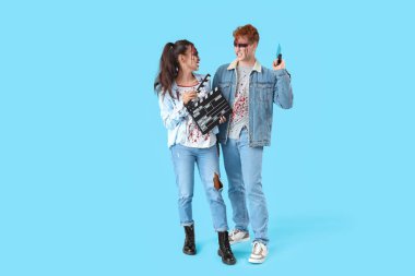 Cadılar Bayramı için giyinmiş korkunç genç çift mavi arka planda film alkışları olan zombiler gibi giyinmiş.