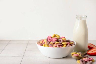 Renkli mısır gevreği halkaları, çilek dilimleri ve beyaz fayans masasında bir şişe süt.