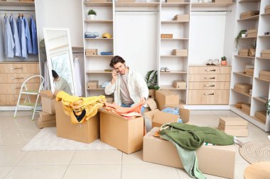 Giysi kutuları ve şık giysileri olan yakışıklı genç adam soyunma odasında cep telefonuyla konuşuyor.