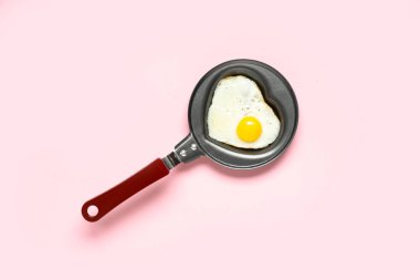 Pembe arka planda kalp şeklinde kızarmış yumurta ile kızartma tavası.