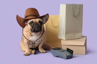 Kovboy şapkası, alışveriş çantaları, kutu ve ödeme terminali olan şirin bir Fransız bulldog.