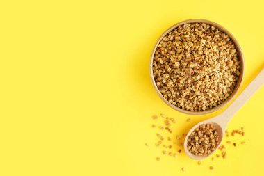 Sarı zemin üzerinde çiğ karabuğday taneleri olan kase