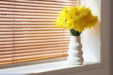 Lamba odasındaki pencere eşiğinde narsis çiçekleri olan vazo.