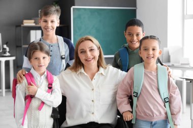 Tekerlekli sandalyedeki olgun öğretmen ve okulda küçük öğrenciler.