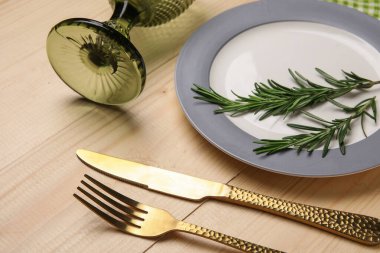 Ahşap zemin üzerinde çatal bıçak, cam ve biberiye ile şık masa ayarları