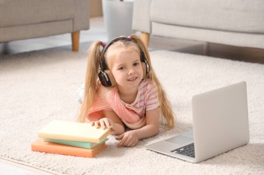 Kulaklıklı şirin kız oturma odasında halıda yatarken modern bilgisayarla sesli kitap dinliyor.