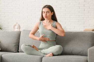 Evdeki kanepede nefes egzersizi yapan güzel bir genç kadın.