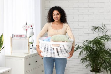Evinde bir sepet temiz elbisesi olan güzel, mutlu, Afro-Amerikalı bir kadın.
