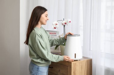 Genç bir kadın odada modern nemlendiriciyi açıyor.