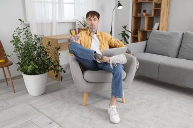 Evdeki koltukta oturan farklı tek kullanımlık elektronik sigaraları olan yakışıklı genç adam.