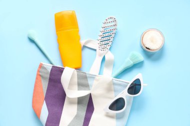 Kozmetik çanta, güneş kremi, tarak, toz ve güneş gözlükleri mavi arka planda