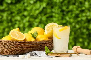 Dışarıdaki beyaz ahşap masada naneli ve meyve sıkacağıyla bir bardak taze limonata.