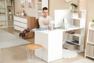 Açık ev ofisinde PC ve tablet bilgisayarla çalışan genç serbest çalışan bir erkek.