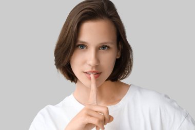 Gri arka planda sessiz jest gösteren sivilceli güzel genç bir kadın.