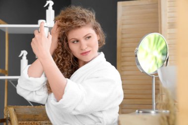 Evdeki banyoya ayna ile saç spreyi sıkan güzel bir genç kadın.