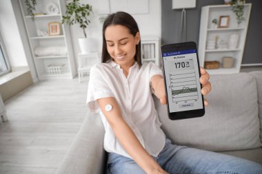 Glikoz sensörü ve cep telefonu olan şeker hastası genç bir kadın evde kan şekeri seviyesini ölçüyor.