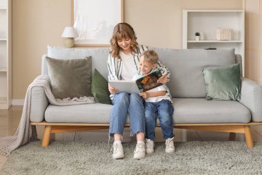 Mutlu anne ve küçük oğlu evdeki kanepede kitap okuyor.