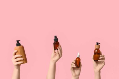 Pembe arka planda farklı kozmetik ürünleri şişeleri olan kadın elleri