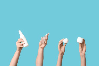 Mavi arka planda şişeler ve kozmetik ürünlerle dolu kadın elleri.