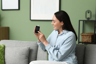 Evdeki kanepede glukometre kullanan şeker hastası genç bir kadın.