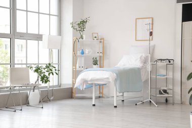 Hastane koğuşunun içinde yatak, serum ve raf ünitesi var.