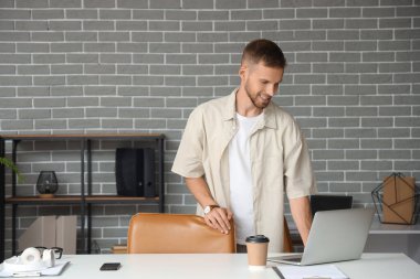 Ofisteki masada dizüstü bilgisayar kullanan genç sakallı adam.