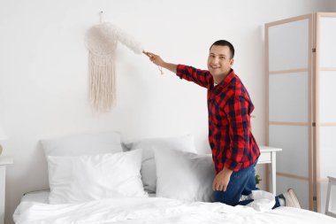 Genç adam yatak odasında duvar halısını temizliyor.