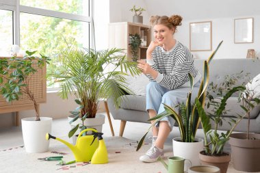 Evde yeşil bitkilerle ilgilenen genç bir kadın.