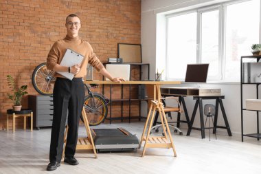 Ofiste koşu bandının yanında panosu olan genç bir işadamı.