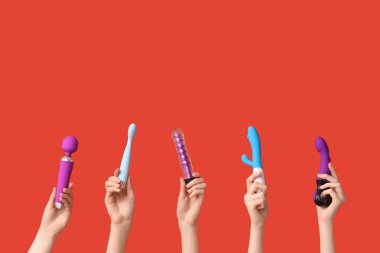 Kırmızı arka planda farklı vibratörlere sahip kadın elleri.