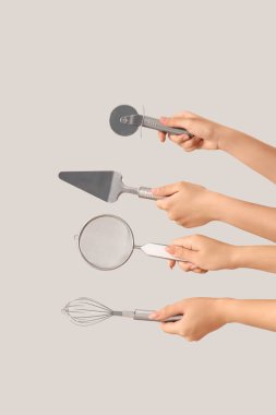 Gri arka planda farklı pişirme aletleri tutan kadın eller.