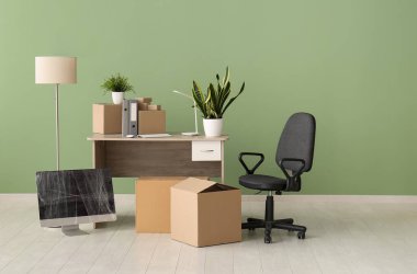 Taşınma gününde iş yerindeki yeşil duvarın yanında karton kutular ve sandalye.