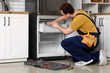 Mutfaktaki buzdolabını tamir eden erkek işçi.