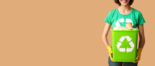 Female volunteer holding recycle bin with garbage on beige background