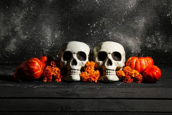 Siyah ahşap masa üzerinde kafatası, kabak ve kadife çiçekli Cadılar Bayramı kompozisyonu