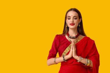 Sarı arka planda dua eden güzel, mutlu, Hintli bir kadın.