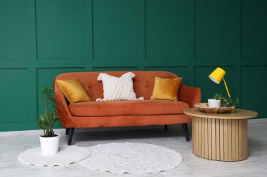 Kahverengi kanepe ve kahve masası lambası yeşil duvarın yanında.